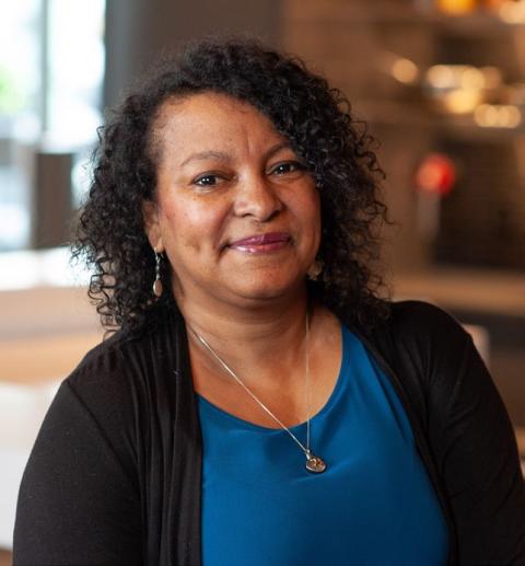 Patricia Gill is a woman with very curly dark hair wearing a nice blouse and cardigan and matching necklace and earrings.