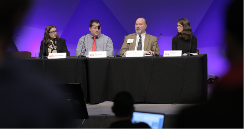 Four people having a discussion on a panel at a conference